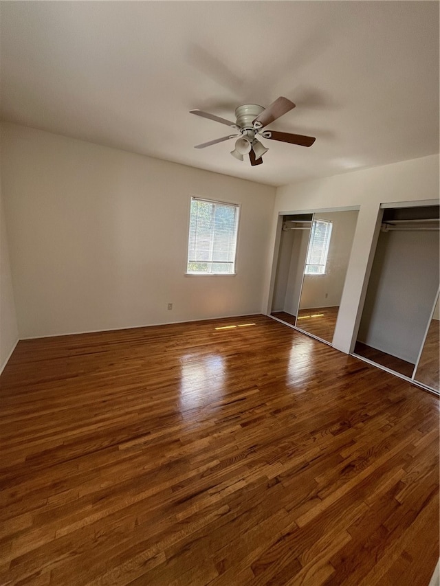 unfurnished bedroom with ceiling fan, two closets, and dark wood-type flooring