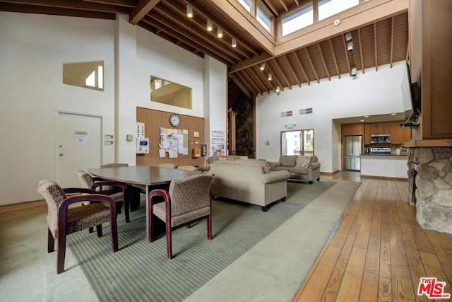 dining space with beam ceiling, high vaulted ceiling, and light hardwood / wood-style flooring