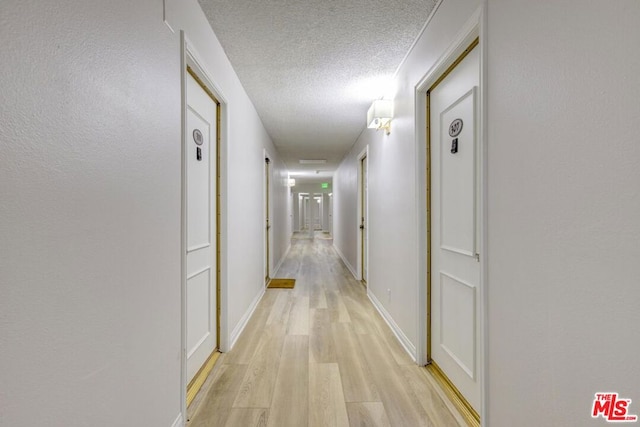 corridor featuring light wood-type flooring and a textured ceiling