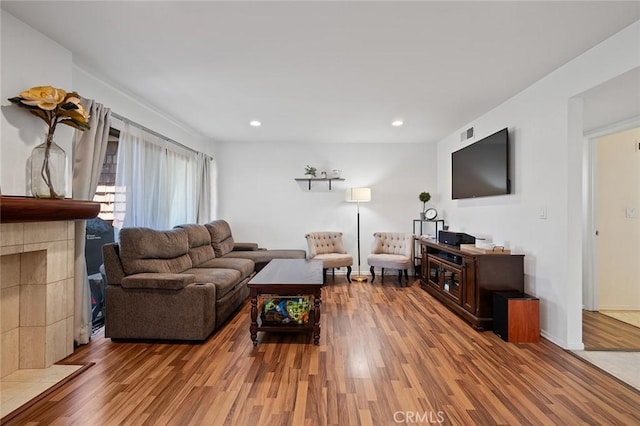 living room featuring wood-type flooring and a tiled fireplace