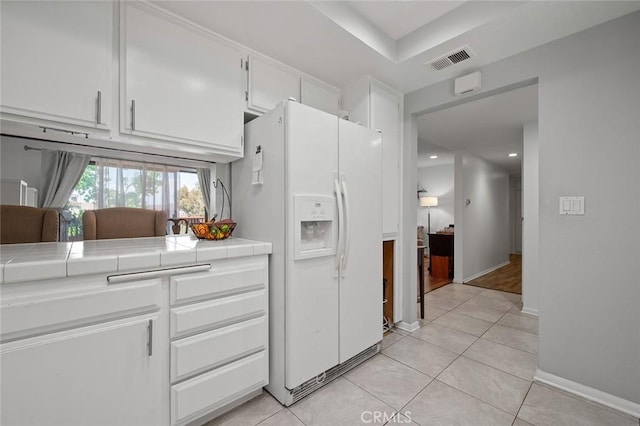 kitchen with light tile patterned floors, white cabinetry, tile counters, and white fridge with ice dispenser