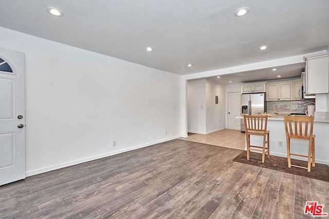 kitchen with kitchen peninsula, a kitchen breakfast bar, stainless steel appliances, decorative backsplash, and hardwood / wood-style floors