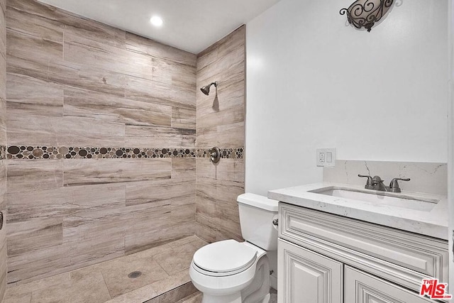 bathroom with a tile shower, vanity, and toilet