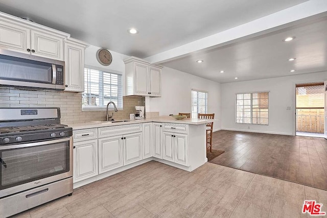 kitchen with sink, kitchen peninsula, plenty of natural light, stainless steel appliances, and light hardwood / wood-style floors