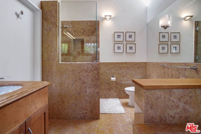 bathroom featuring tile walls, vanity, a tile shower, tile patterned flooring, and toilet