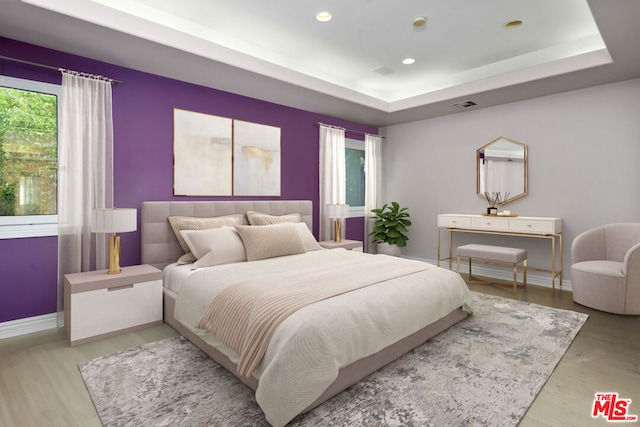 bedroom with light wood-type flooring and a raised ceiling