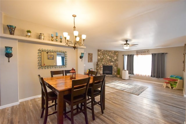 dining area featuring ceiling fan with notable chandelier, wood-type flooring, and a fireplace