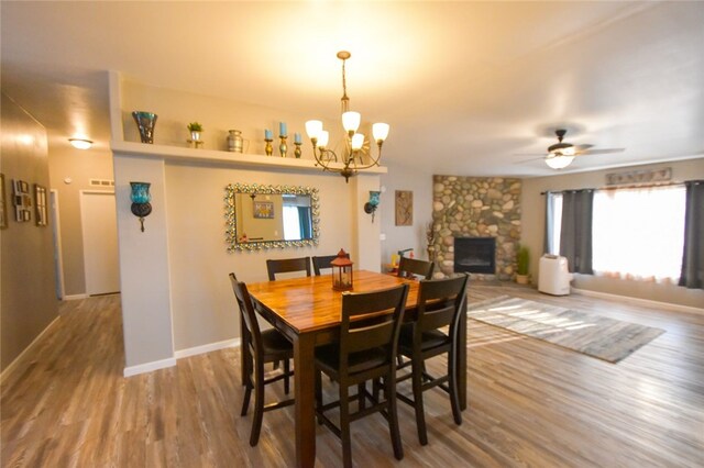 dining space with hardwood / wood-style flooring, ceiling fan with notable chandelier, and a fireplace