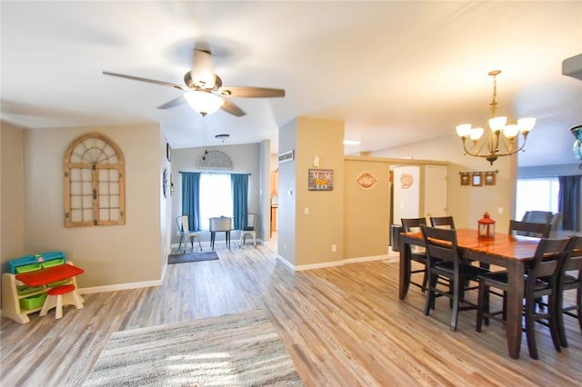 dining space with ceiling fan with notable chandelier, light hardwood / wood-style flooring, plenty of natural light, and lofted ceiling