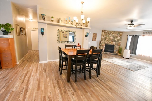 dining space featuring ceiling fan with notable chandelier, light wood-type flooring, and a stone fireplace