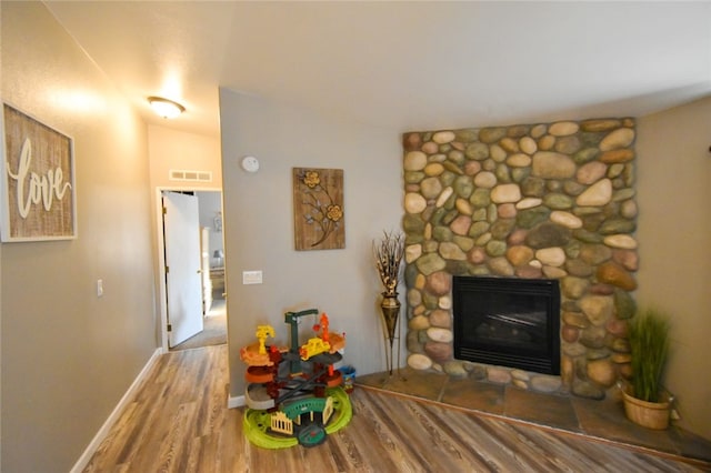 living room with wood-type flooring, a stone fireplace, and vaulted ceiling