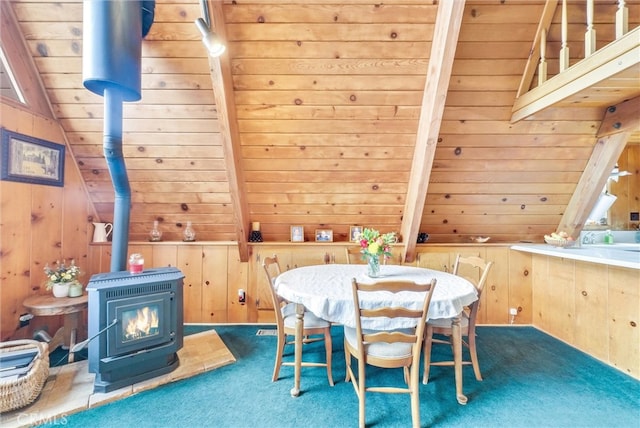 carpeted dining space with lofted ceiling, wood walls, wooden ceiling, and a wood stove