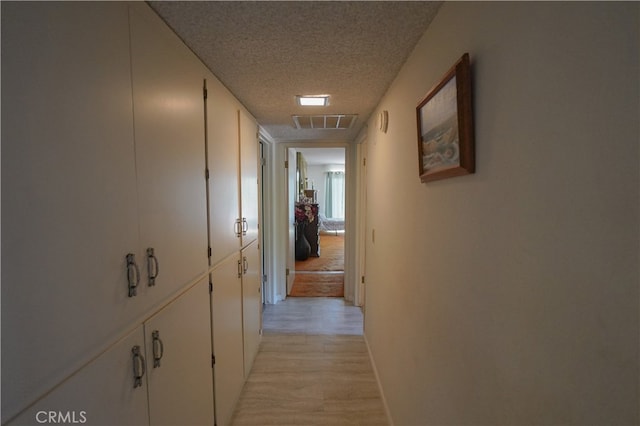 corridor with a textured ceiling and light hardwood / wood-style flooring