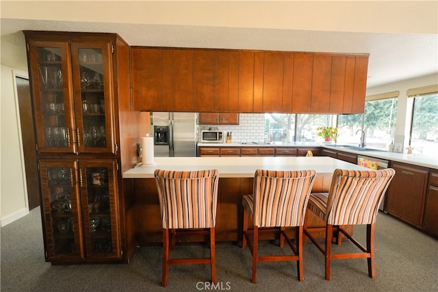 kitchen featuring dark carpet, sink, backsplash, stainless steel appliances, and a breakfast bar area