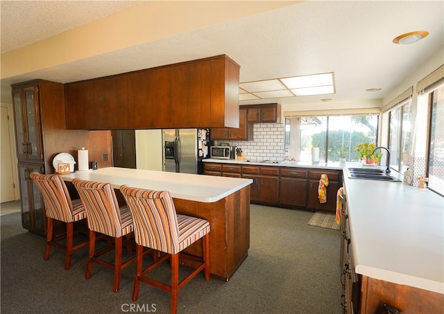 kitchen featuring backsplash, kitchen peninsula, a breakfast bar area, stainless steel appliances, and sink