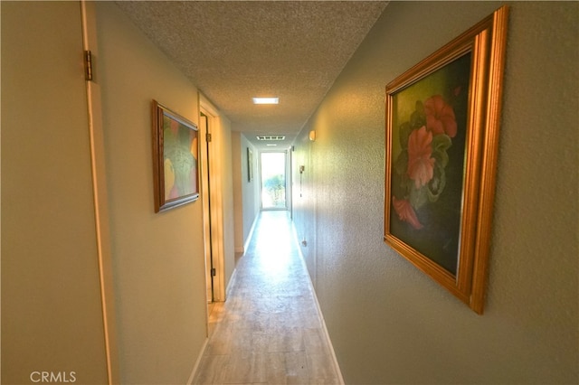 corridor with a textured ceiling and light hardwood / wood-style flooring