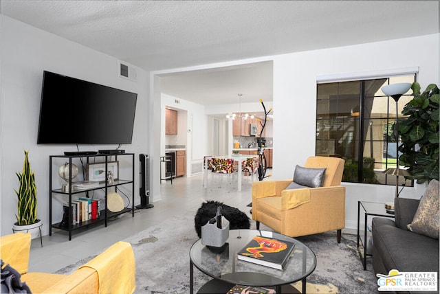 living room with a textured ceiling, an inviting chandelier, light tile patterned floors, and beverage cooler