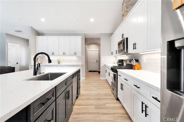 kitchen with light stone countertops, stainless steel appliances, white cabinetry, and sink