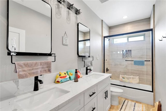 full bathroom with wood-type flooring, shower / bath combination with glass door, vanity, and toilet