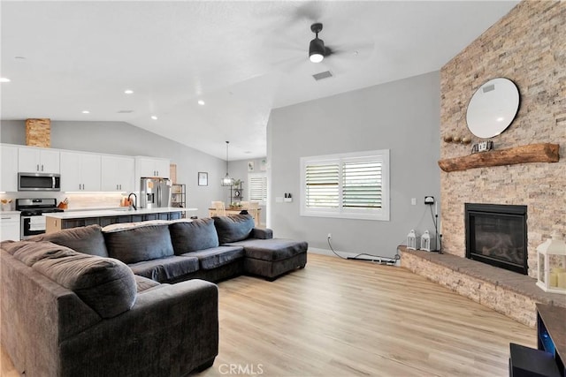 living room featuring a stone fireplace, ceiling fan, lofted ceiling, light hardwood / wood-style flooring, and sink