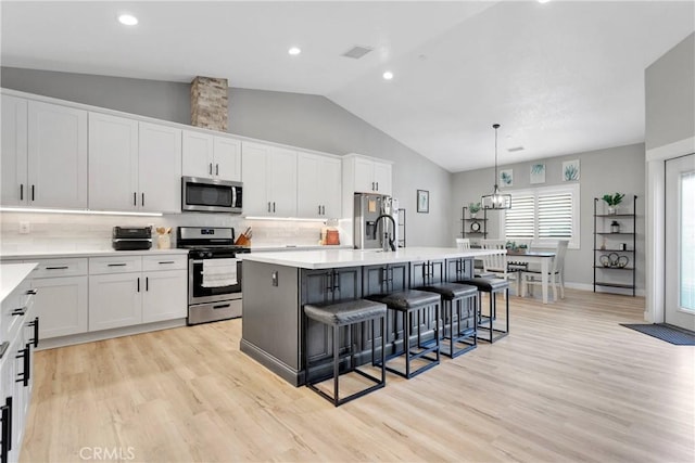 kitchen featuring decorative light fixtures, decorative backsplash, white cabinetry, a kitchen island with sink, and appliances with stainless steel finishes