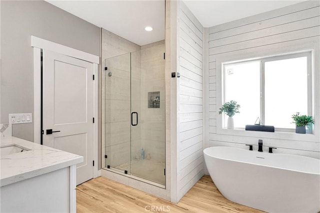 bathroom with wood walls, independent shower and bath, hardwood / wood-style floors, and vanity