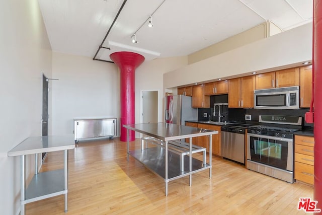 kitchen with appliances with stainless steel finishes, rail lighting, light hardwood / wood-style floors, backsplash, and sink