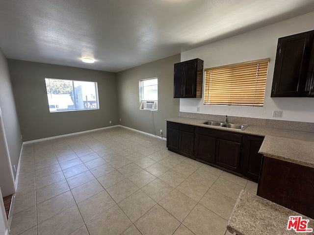 kitchen featuring dark brown cabinetry, cooling unit, light tile patterned flooring, and sink