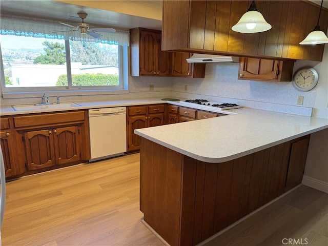 kitchen featuring kitchen peninsula, decorative light fixtures, light wood-type flooring, white appliances, and sink