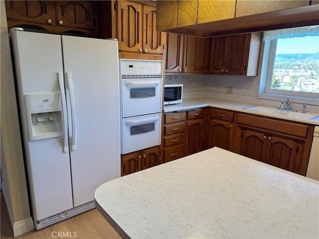 kitchen with sink, light hardwood / wood-style flooring, backsplash, and white appliances