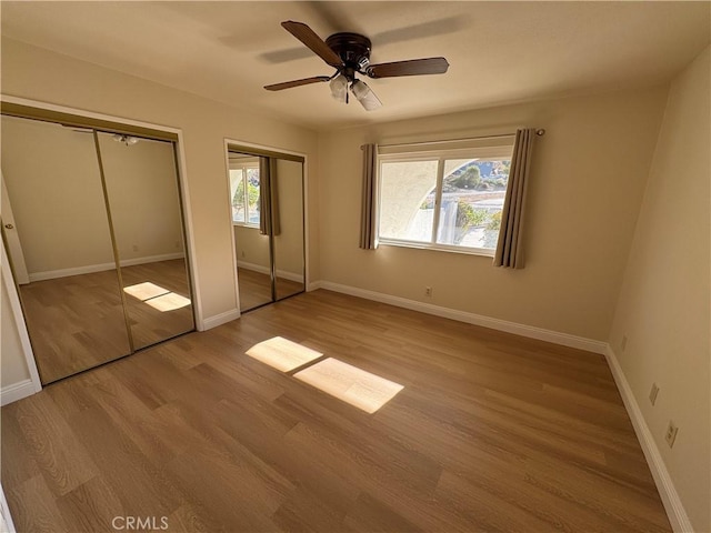 unfurnished bedroom with ceiling fan, light wood-type flooring, and multiple closets