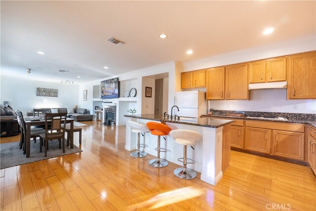 kitchen with an island with sink, white refrigerator, a kitchen bar, and light hardwood / wood-style flooring