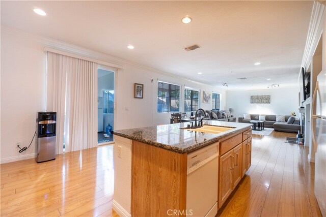 kitchen featuring white dishwasher, sink, a center island with sink, light hardwood / wood-style flooring, and dark stone counters