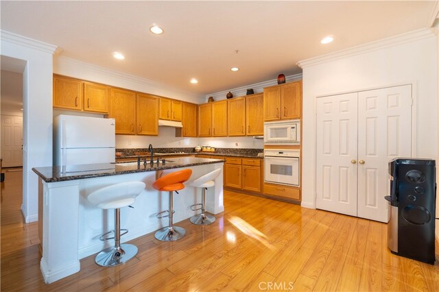 kitchen featuring ornamental molding, white appliances, a kitchen island with sink, a breakfast bar, and light wood-type flooring