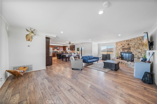 living room featuring ceiling fan, a stone fireplace, crown molding, and light hardwood / wood-style floors