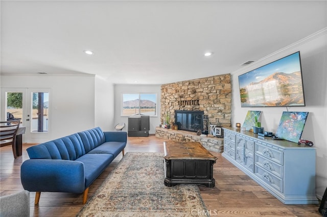 living room with a stone fireplace, wood-type flooring, french doors, and crown molding