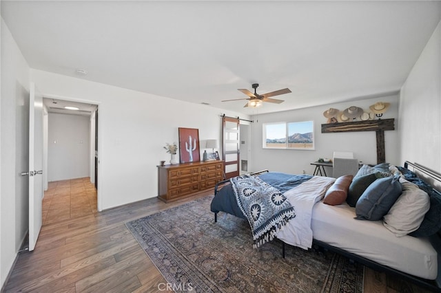 bedroom featuring a barn door, hardwood / wood-style floors, and ceiling fan