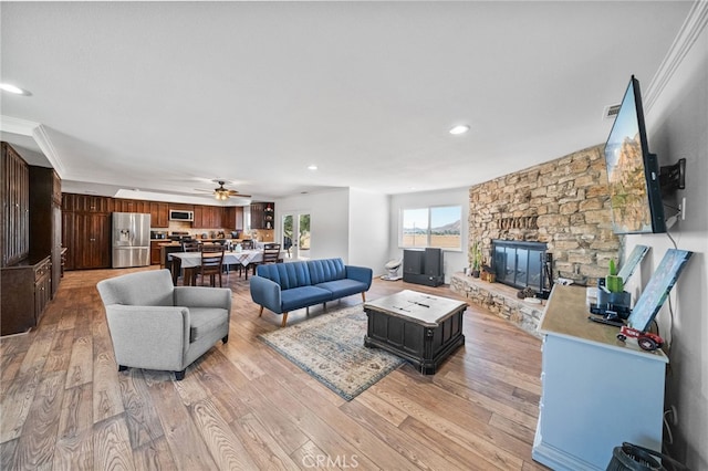 living room with ceiling fan, a fireplace, crown molding, and light hardwood / wood-style floors