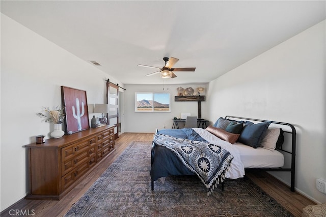 bedroom with a barn door, dark hardwood / wood-style floors, and ceiling fan