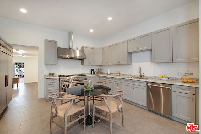 kitchen featuring sink, high end appliances, wall chimney range hood, gray cabinetry, and light stone countertops