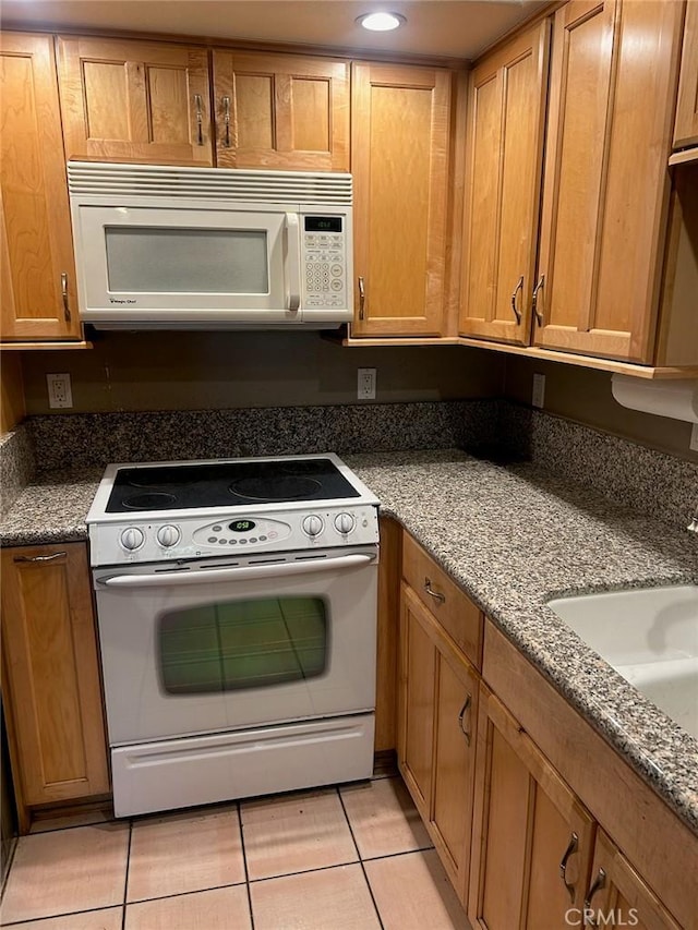 kitchen featuring light tile patterned floors, white appliances, dark stone counters, and sink