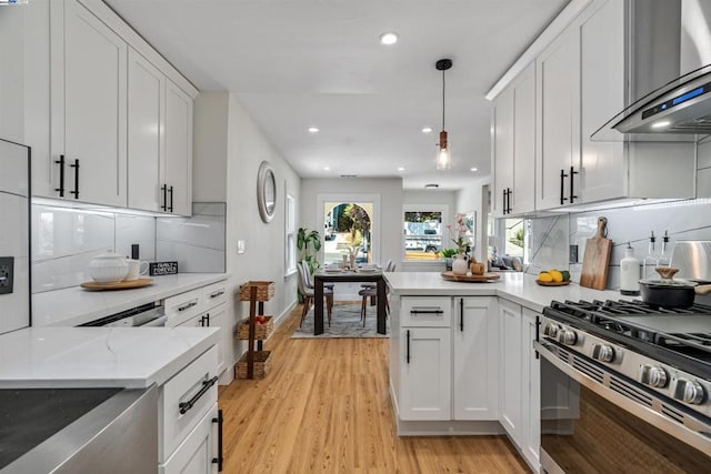 kitchen with hanging light fixtures, wall chimney range hood, white cabinets, and light hardwood / wood-style flooring