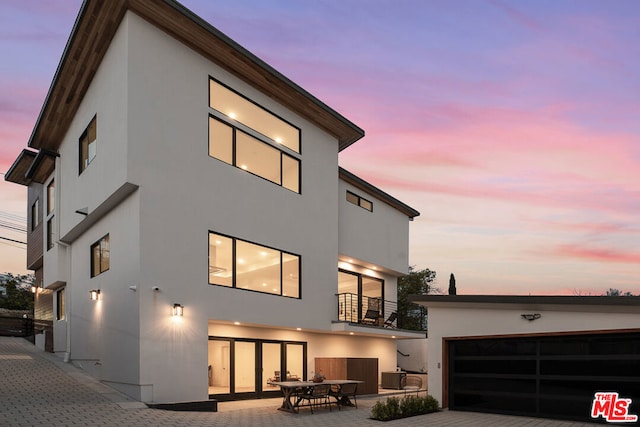 back house at dusk featuring a balcony, central AC unit, and a garage