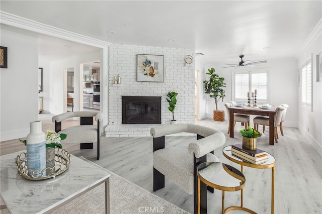 living room featuring light hardwood / wood-style flooring, a brick fireplace, ceiling fan, and ornamental molding