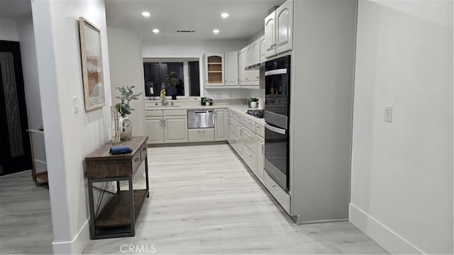 kitchen featuring stainless steel gas stovetop, white cabinets, light hardwood / wood-style floors, and sink