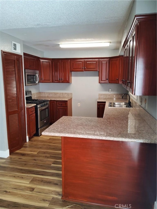 kitchen with kitchen peninsula, sink, dark hardwood / wood-style floors, and appliances with stainless steel finishes