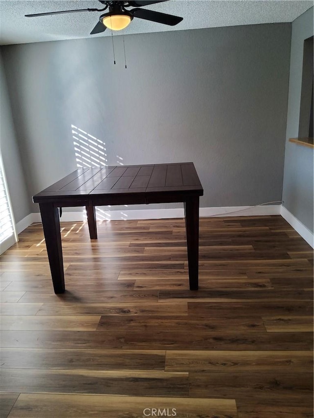 unfurnished dining area with ceiling fan, dark wood-type flooring, and a textured ceiling