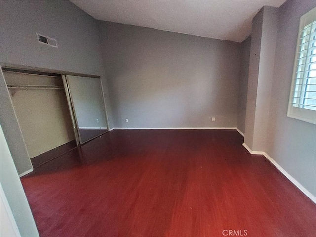 unfurnished bedroom featuring dark hardwood / wood-style flooring, lofted ceiling, and a closet