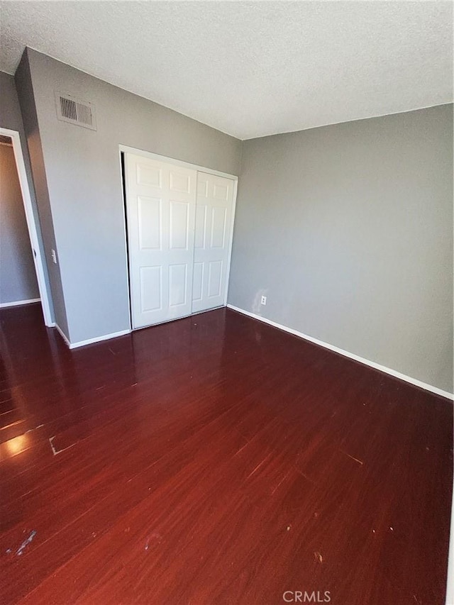 unfurnished bedroom featuring a textured ceiling, a closet, and dark hardwood / wood-style floors