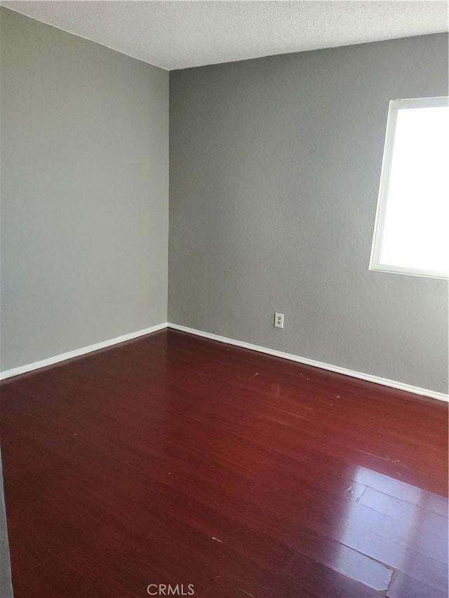 unfurnished room with a textured ceiling and dark wood-type flooring